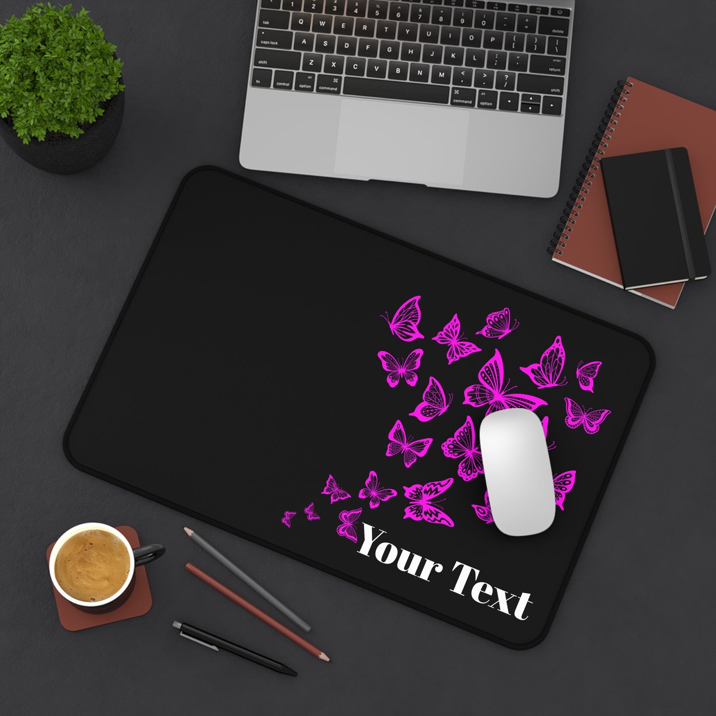 Black mouse pad with pink butterfly design and 'Your Text' placeholder on a desk with laptop, coffee, and stationery.