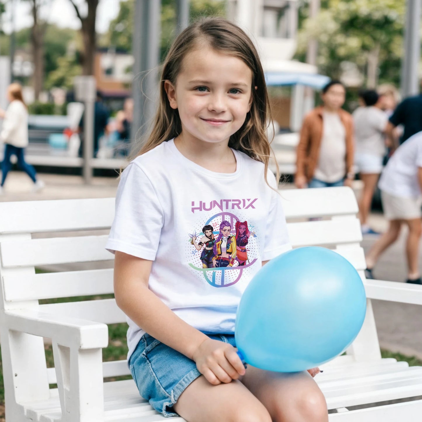 Young girl sitting on a bench holding a blue balloon, wearing a white t-shirt with a graphic design.