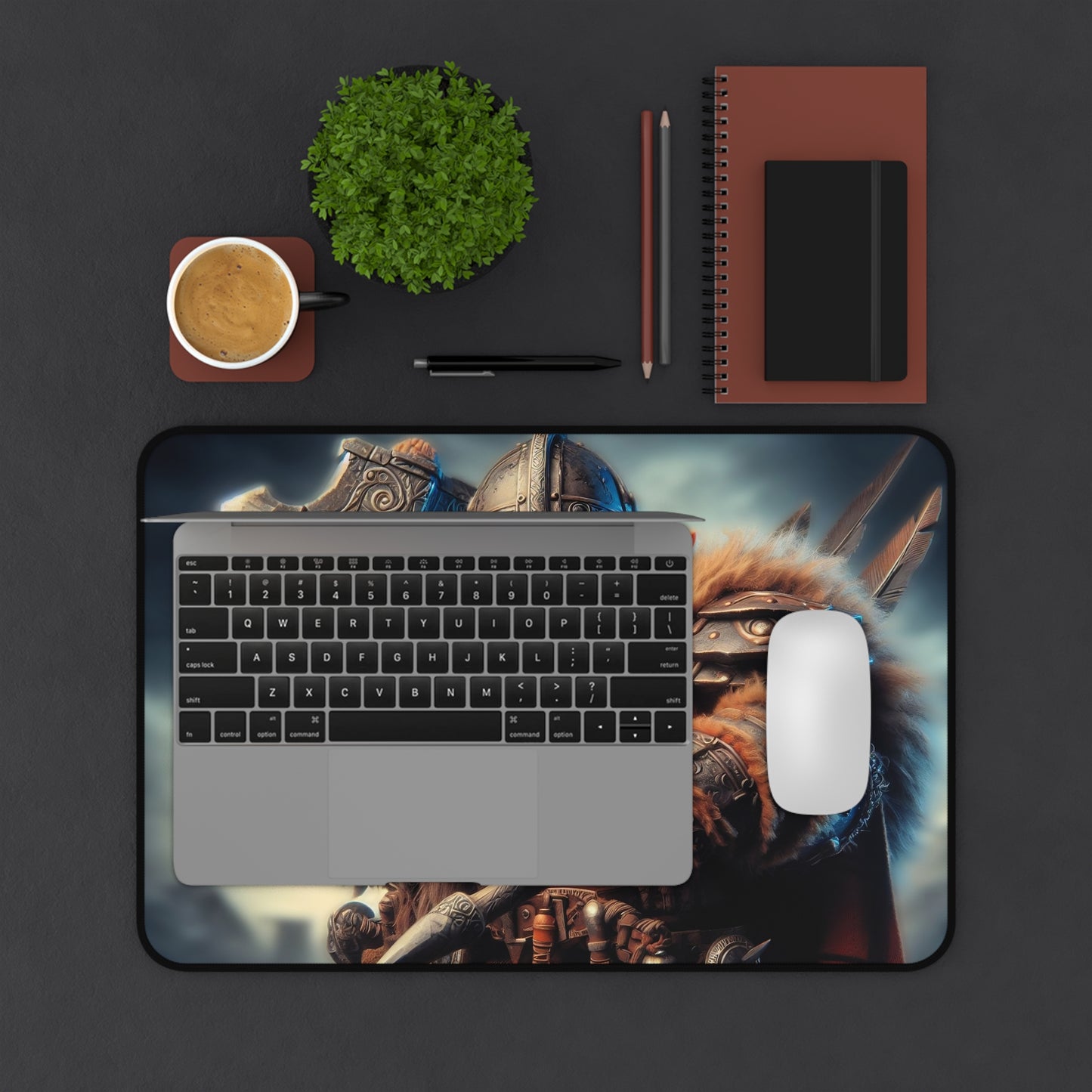 Laptop with a dragon-themed mouse pad on a dark surface with office items.