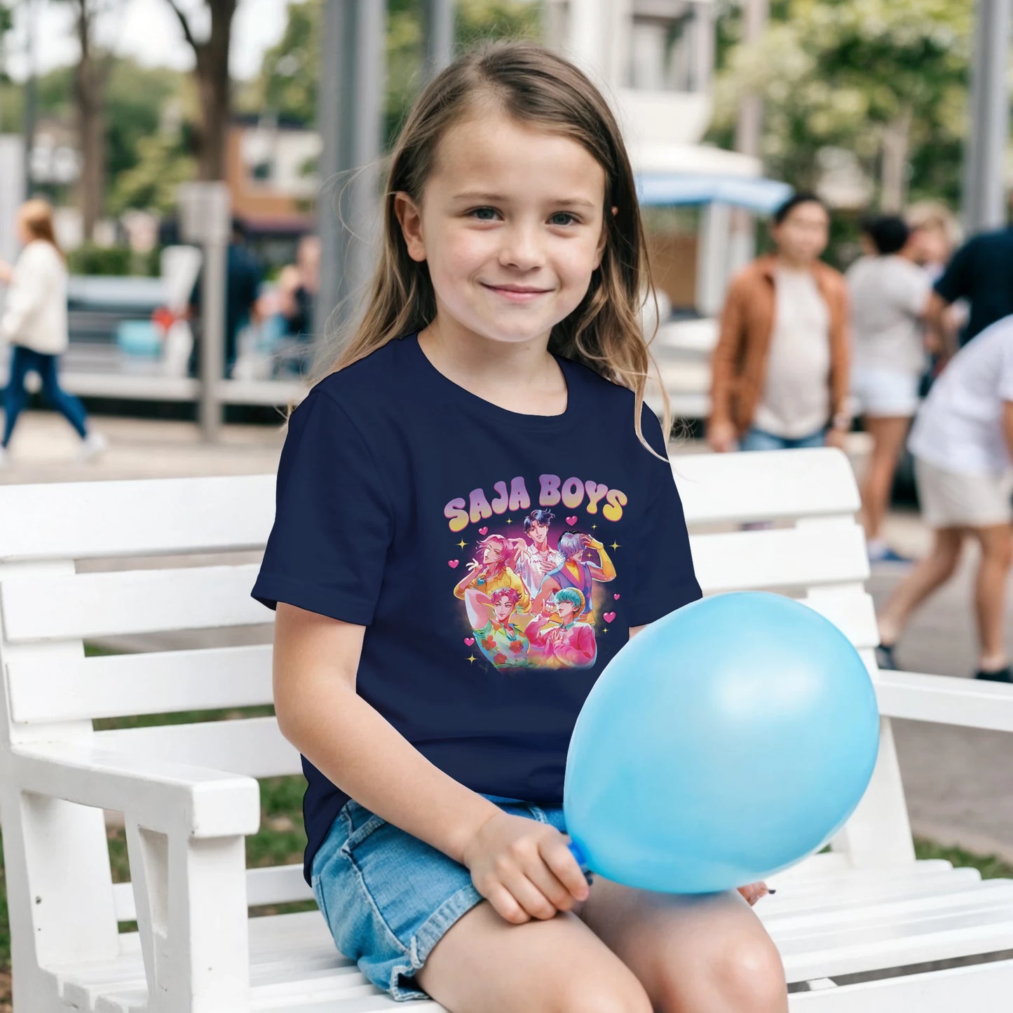 Young girl sitting on a bench holding a blue balloon, wearing a navy blue t-shirt with colorful graphics and text.