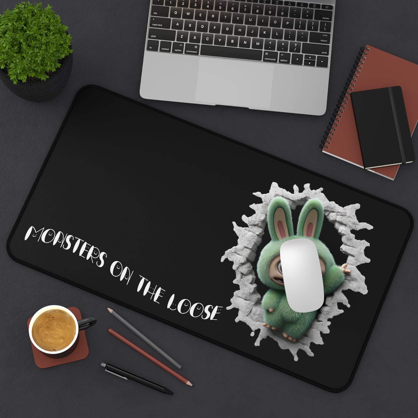 Desk setup with a black mouse pad featuring a green labubu monster design and text 'MONSTERS ON THE LOOSE'.