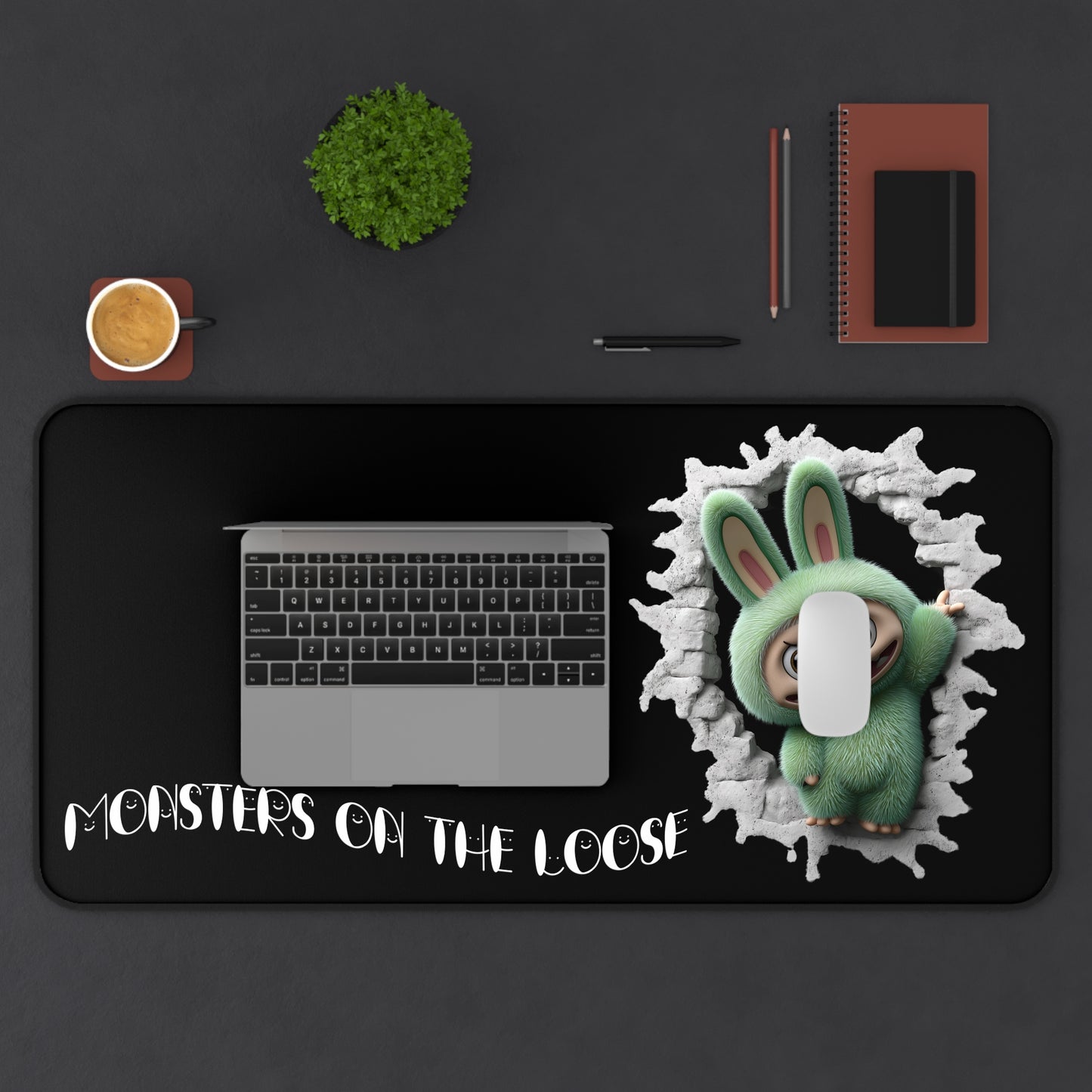 Desk setup with a laptop, notebook, and cup on a black desk mat featuring a cartoon labubu monster character and text.
