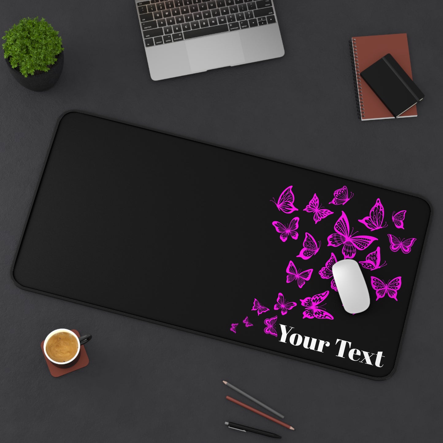Black desk mat with pink butterflies and 'Your Text' placeholder on a dark surface with office items.
