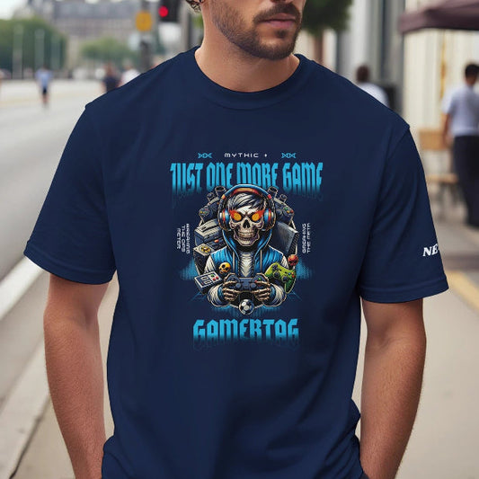 Man wearing a navy blue t-shirt with a graphic design of a skelton holding controler, with pc and consoles behind him, thext above the picture reads 'Mythic +' below reads 'Just one more game' on the left side of the picture in smaller text it reads ' breaking the dps meter' on the right side of the picture it reads ' breaking the meta, on a city street