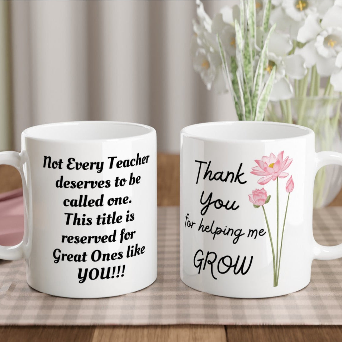 Two glossy white ceramic mugs with personalized text and floral designs, one with text 'Not Every Teacher Deserves To Be Called Great, But Every Teacher Deserves To Be Thanked!' and the other with text 'Not Every Student Grows Up To Be Great, But Every Student Grows With The Help Of A Great Teacher!' placed on a table with a floral arrangement in the background.