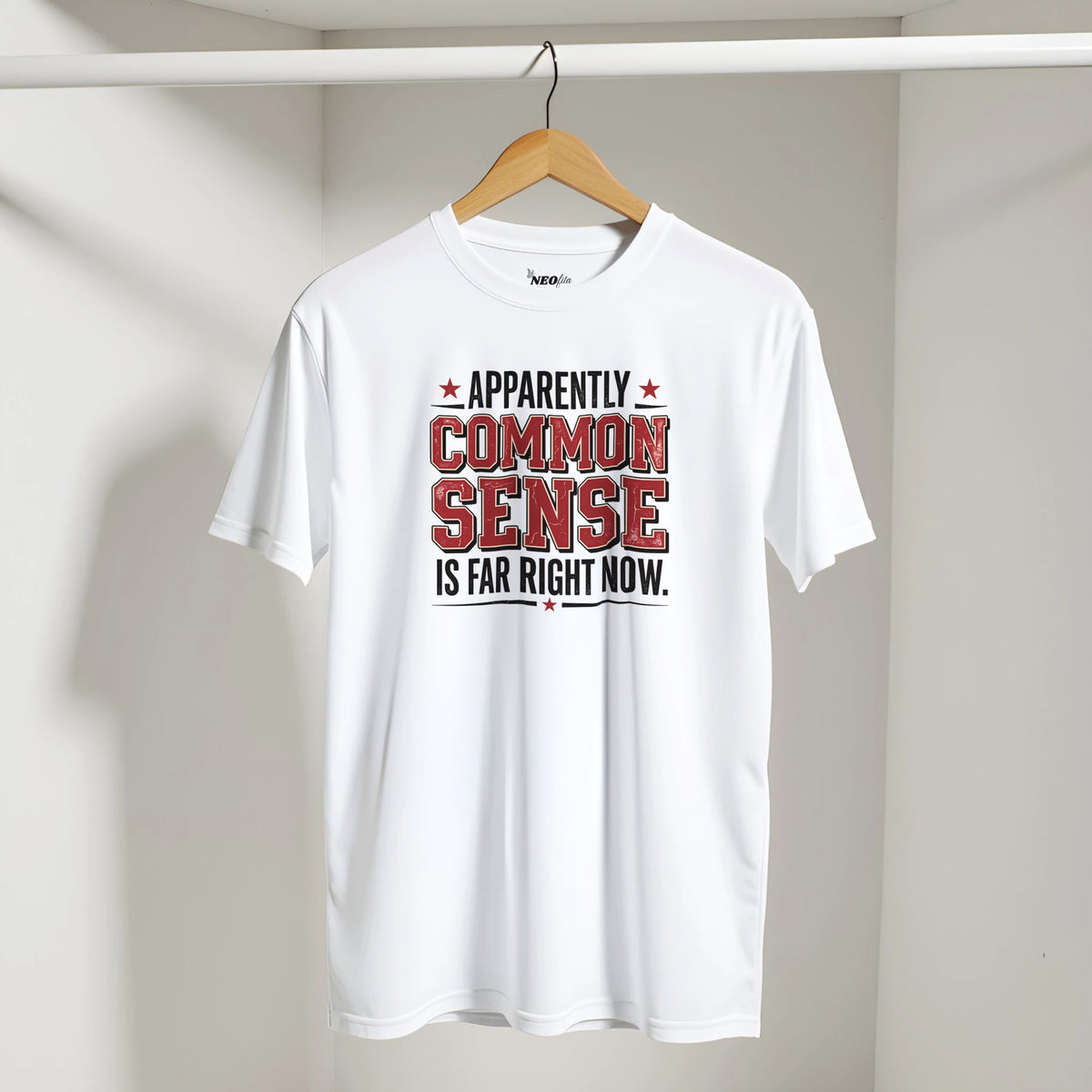A white short-sleeve t-shirt hanging on a wooden hanger against a light gray wall. The shirt features a graphic print on the chest with the text 'APPARENTLY COMMON SENSE IS FAR RIGHT NOW.