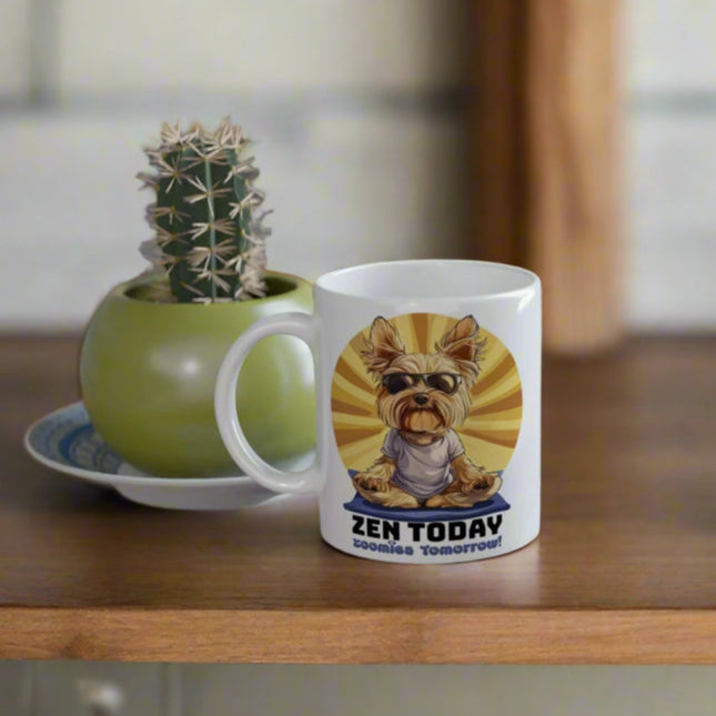 left side view of a funny yorkie mug in a yoga pose with text 'zen today zoomies tomorrow' on the table and coaster, with cactus behind