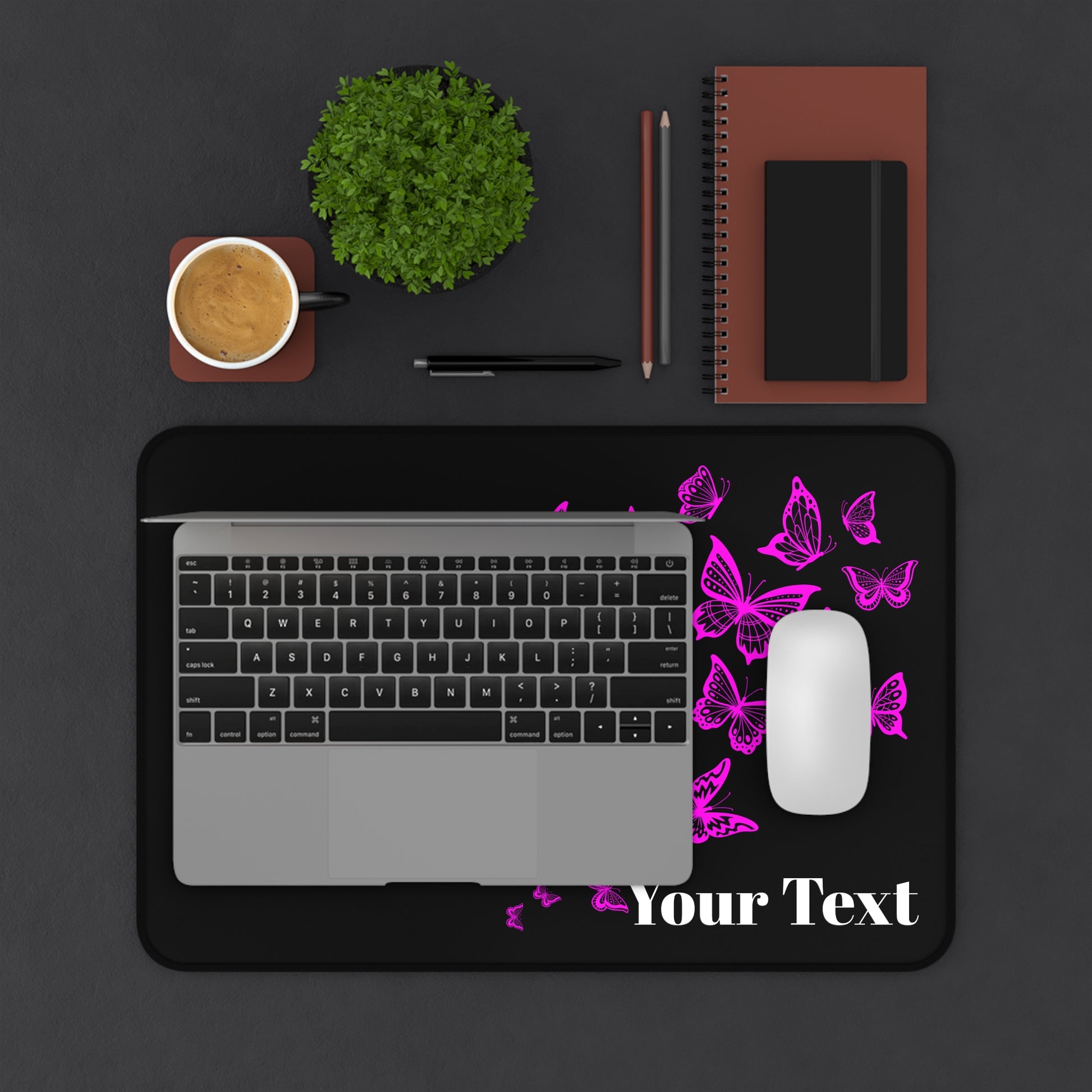 Laptop on a black mouse pad with pink butterflies and 'Your Text' placeholder, surrounded by office supplies on a dark surface.
