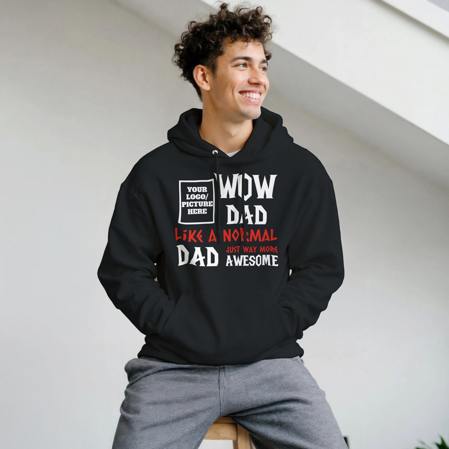 Man wearing a black hoodie with text design, sitting on a white wall.
